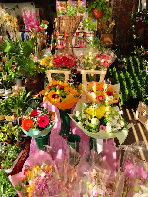 A vibrant display of freshly arranged flower bouquets on a pink table at a florist shop, showcasing a variety of colorful floral arrangements. The bouquets include bright yellow, red, pink, and white