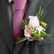 There's a heartfelt elegance in this buttonhole, tailored for a Kenton wedding or prom against the verdant backdrop of Woodcock Park. The wearer's charcoal jacket and vibrant magenta tie frame the scene, but it's the boutonniere's delicate palette that captivates: a softly blushed pink rose, gently unfurling its petals, sits alongside a smaller flower-the pink and purple striations of a miniature lily-or alstroemeria adding intricacy. Wisps of pure white baby's breath cluster around the main blooms, offering a breath of freshness and hope, while a richly green button mum provides an unexpected jolt of colour and texture. Fern fronds and slender leaves bring a feathery complexity, their soft touch reminiscent of Kenton's peaceful corners. Every floral element is chosen with fresh, local expertise, making the boutonniere seem handpicked from the area's bright gardens. The stem is neatly wrapped with a gleaming lavender ribbon bow, reflecting the festive spirit in both hue and finish. Crafted with care by florists who know Kenton's traditions and trends, this arrangement transforms a suit into a story-a celebration of affection, memory, and community, made tangible in petal, scent, and gentle artistry.